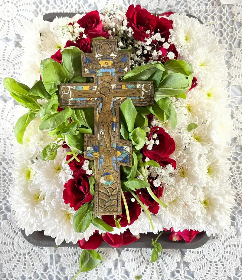 A blessing cross resting on a bed of white and red flowers